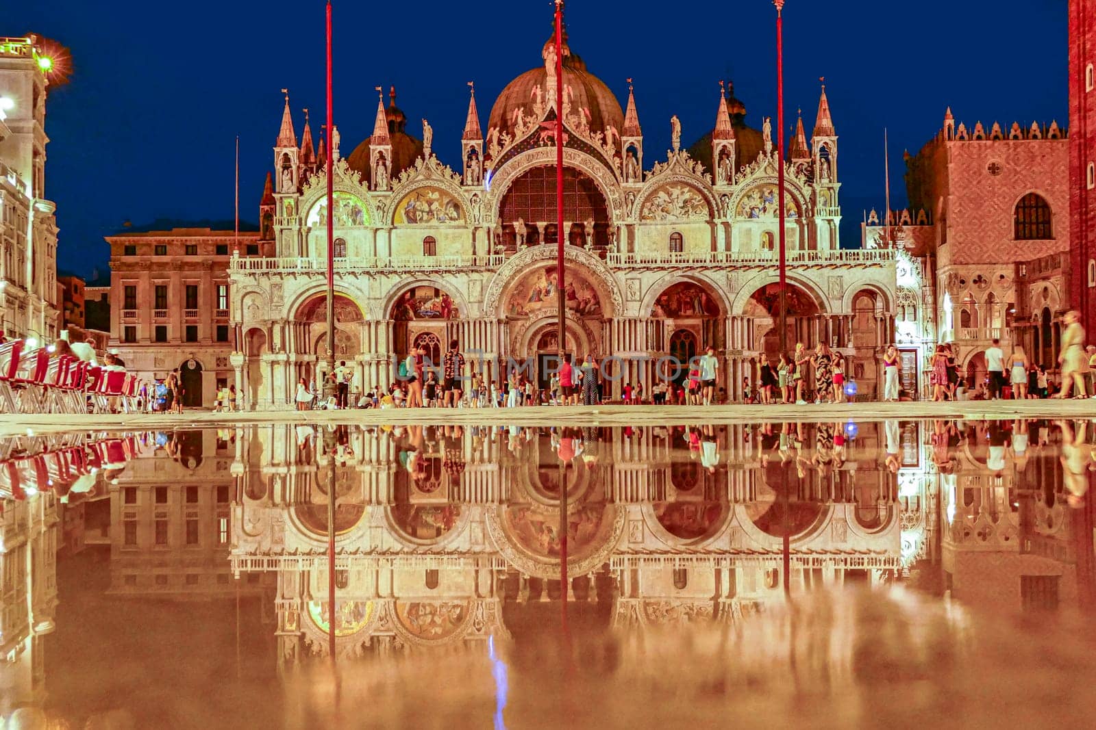 Venice, Italy - July 7, 2021: tourists at the square St. Marco by night with reflection of famous st. Marks cathedral.