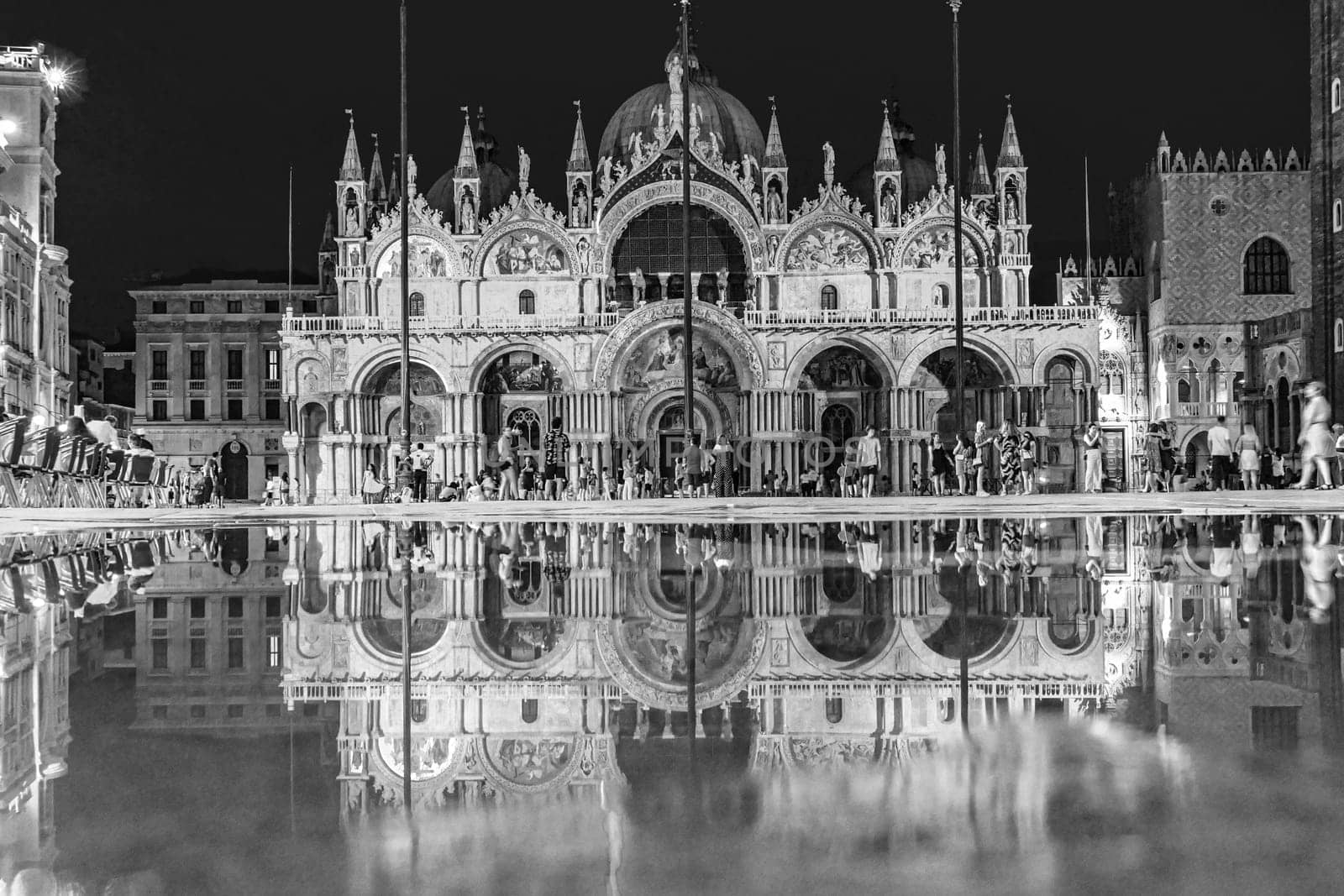 Venice, Italy - July 7, 2021: tourists at the square St. Marco by night with reflection of famous st. Marks cathedral.
