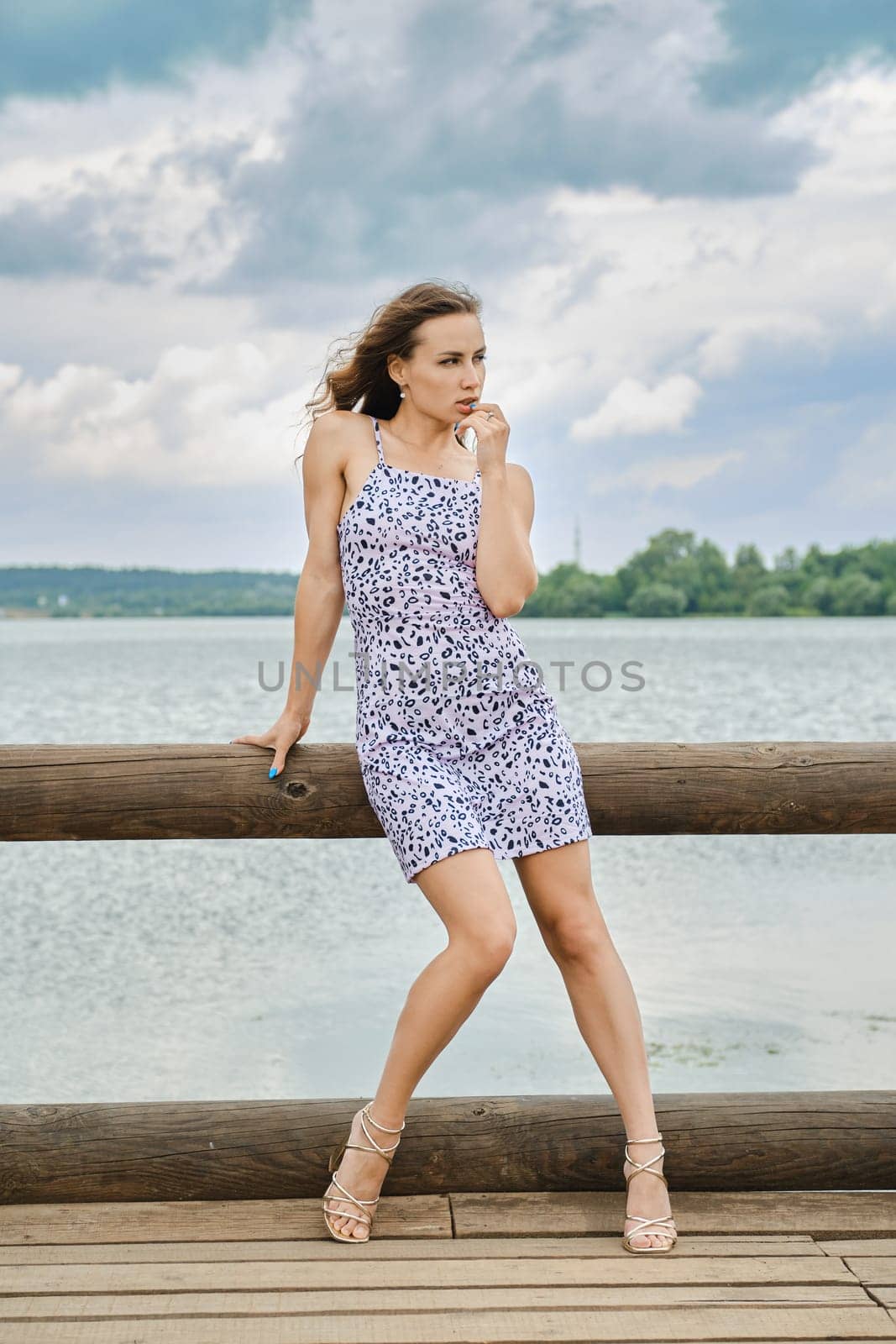 Pensive young woman touching her lip and looking away while standing on pier