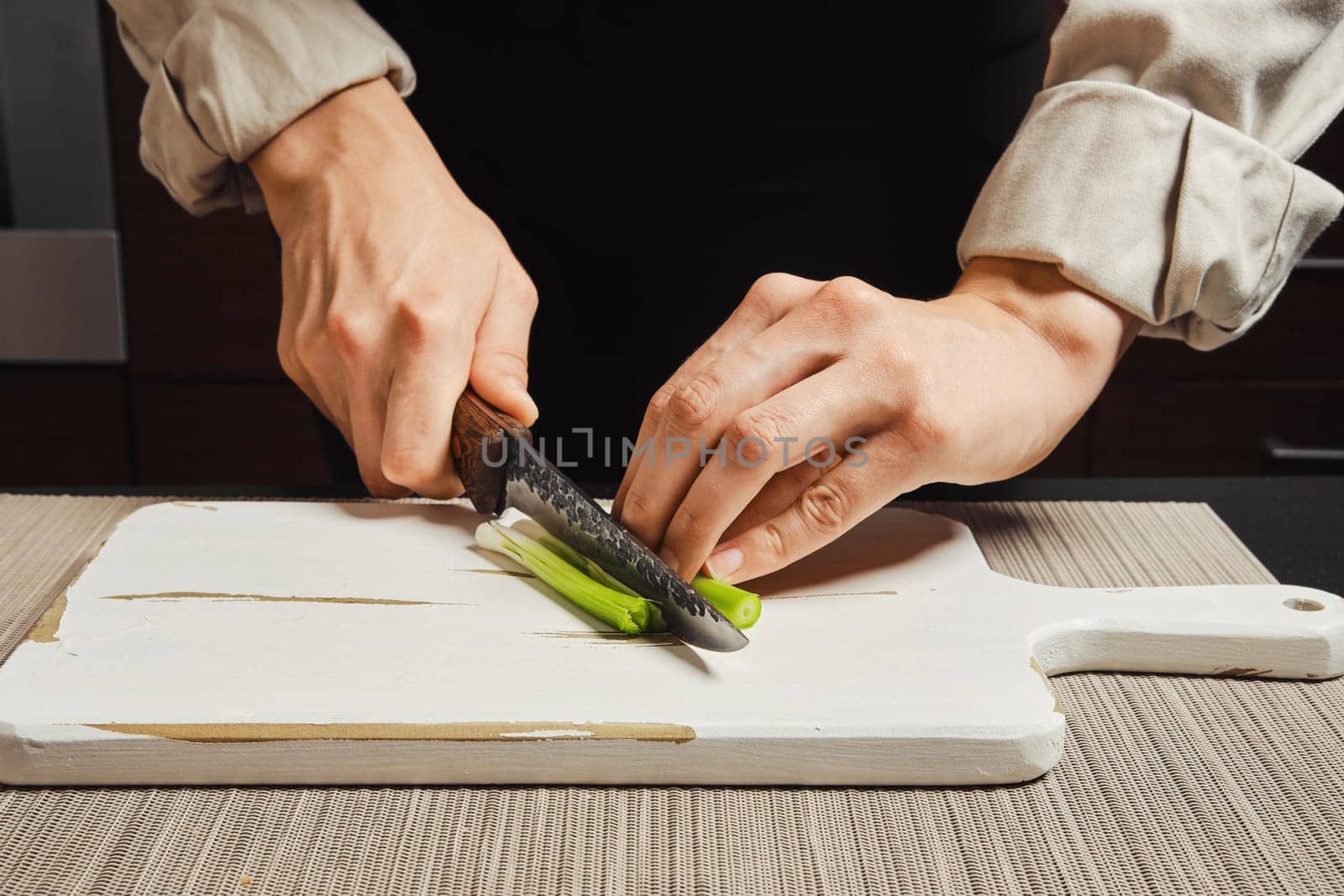 Unrecognizable woman slicing spring onion into thin strips