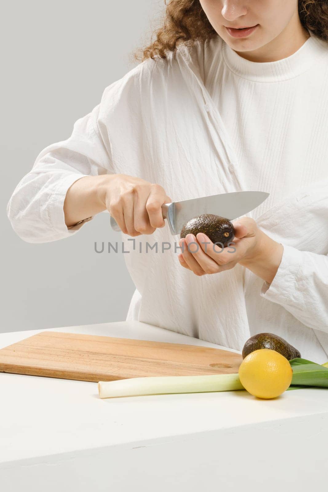 Unrecognizable woman cutting fresh avocado into halves. Concept of balanced eating.