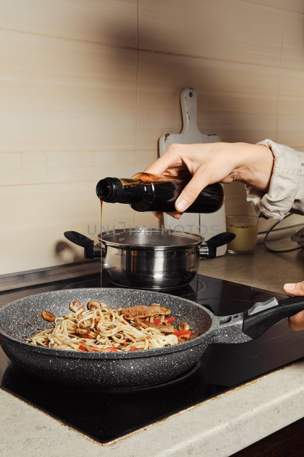 Unrecognizable woman pouring oyster sauce into noodles in a frying pan