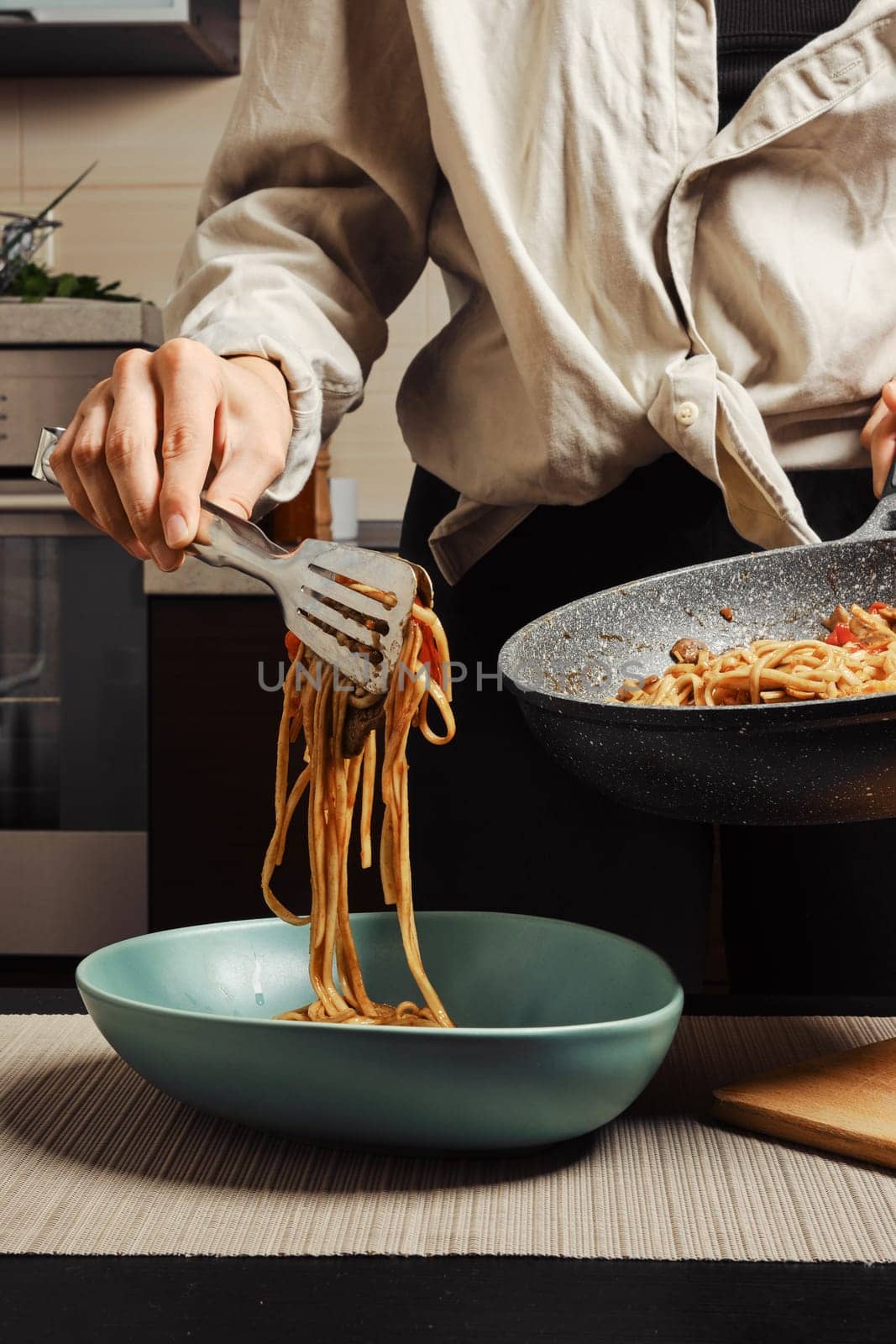 Unrecognizable woman serving rice noodles with vegetables and beef from frying pan into plate