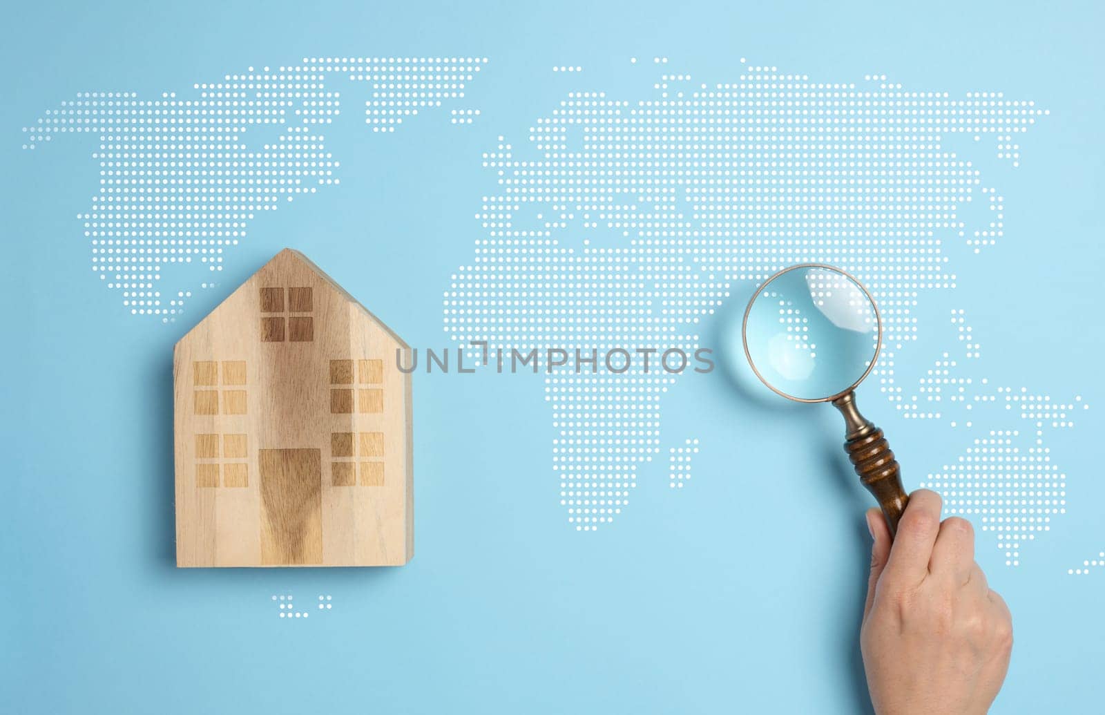 Wooden house on a world map background with a person's hand holding a magnifying glass, symbolizing the concept of searching for a country to move to