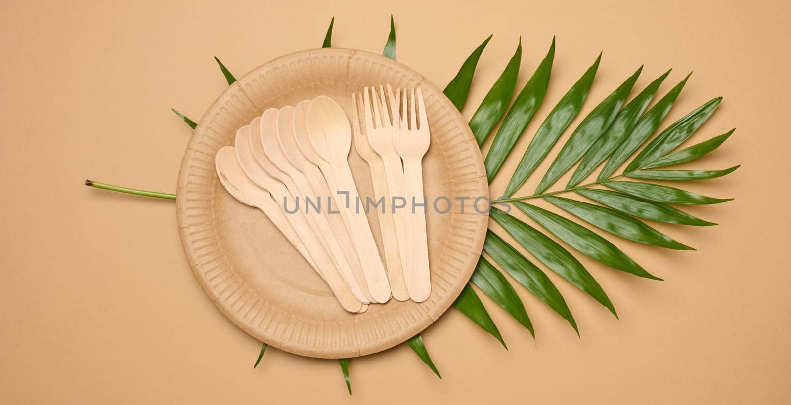 Paper plates, wooden spoons and forks on a beige background, top view