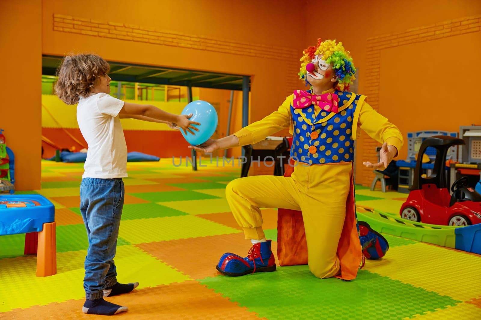 Funny playful games with clown at indoor playroom for children. Happy boy child and artist enjoying creative show with balloons at birthday party. Holiday celebration for kids concept