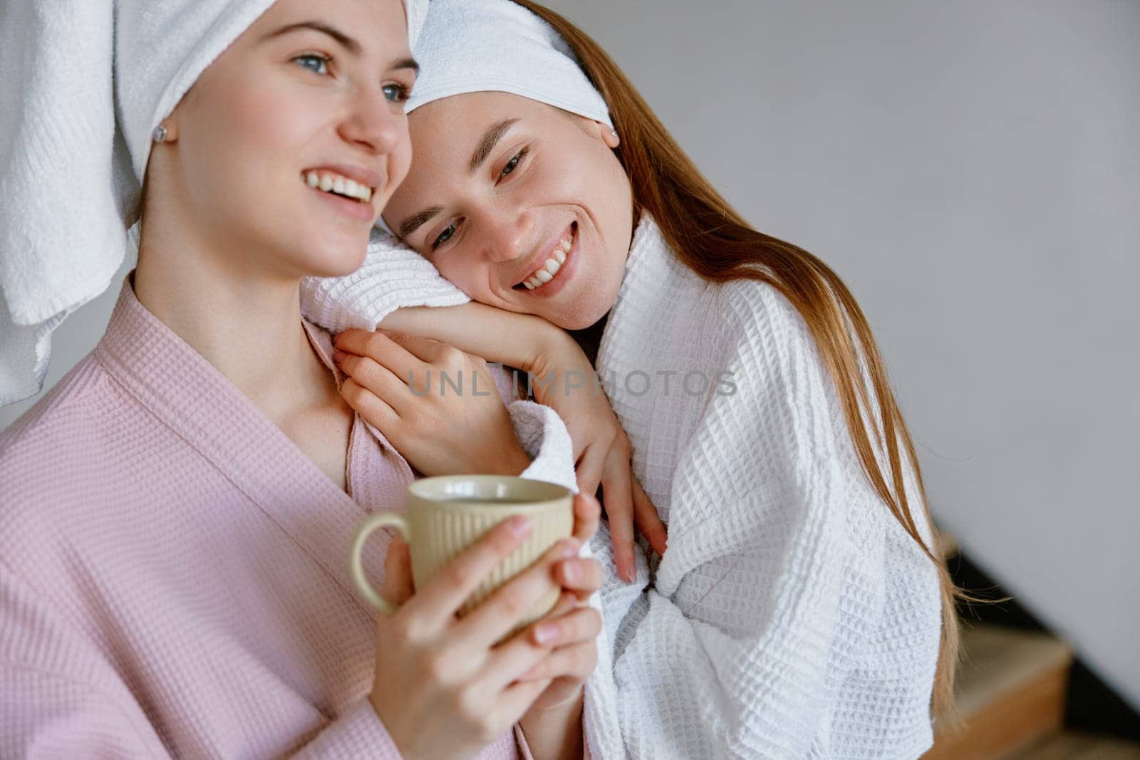 Young two girl friends or sisters wearing bathrobe hugging enjoying morning time together. Friendship and sisterhood, good relationships and bonding concept