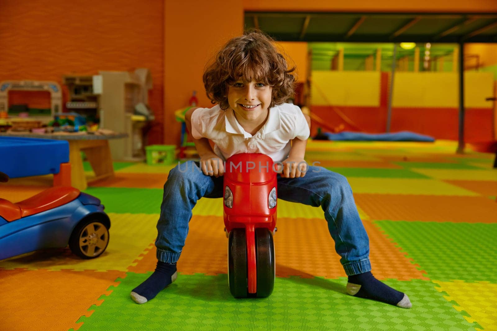 Little enthusiastic boy child playing at playroom. Portrait of male child riding toy motorcycle enjoying happy childhood at amusement area