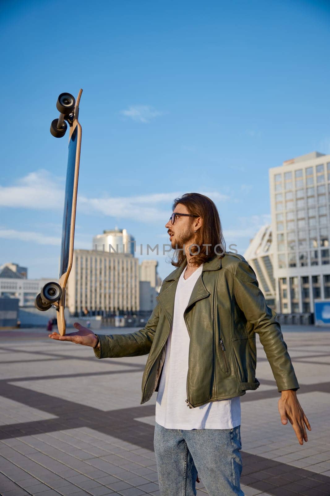 Hipster guy holding skateboard on hand in balance doing trick. Cool teenager man enjoying urban style outdoors