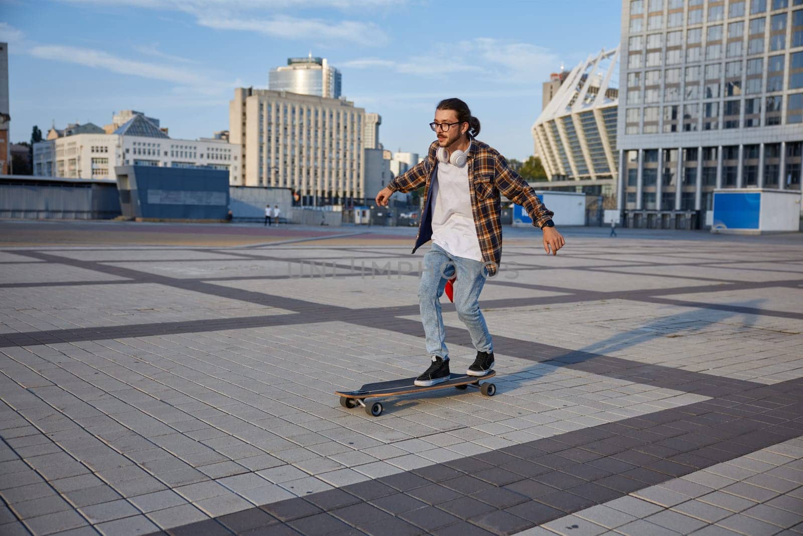 Active energetic stylish hipster guy riding skateboard on city street. Serious young sporty casual man enjoying extreme race on longboard