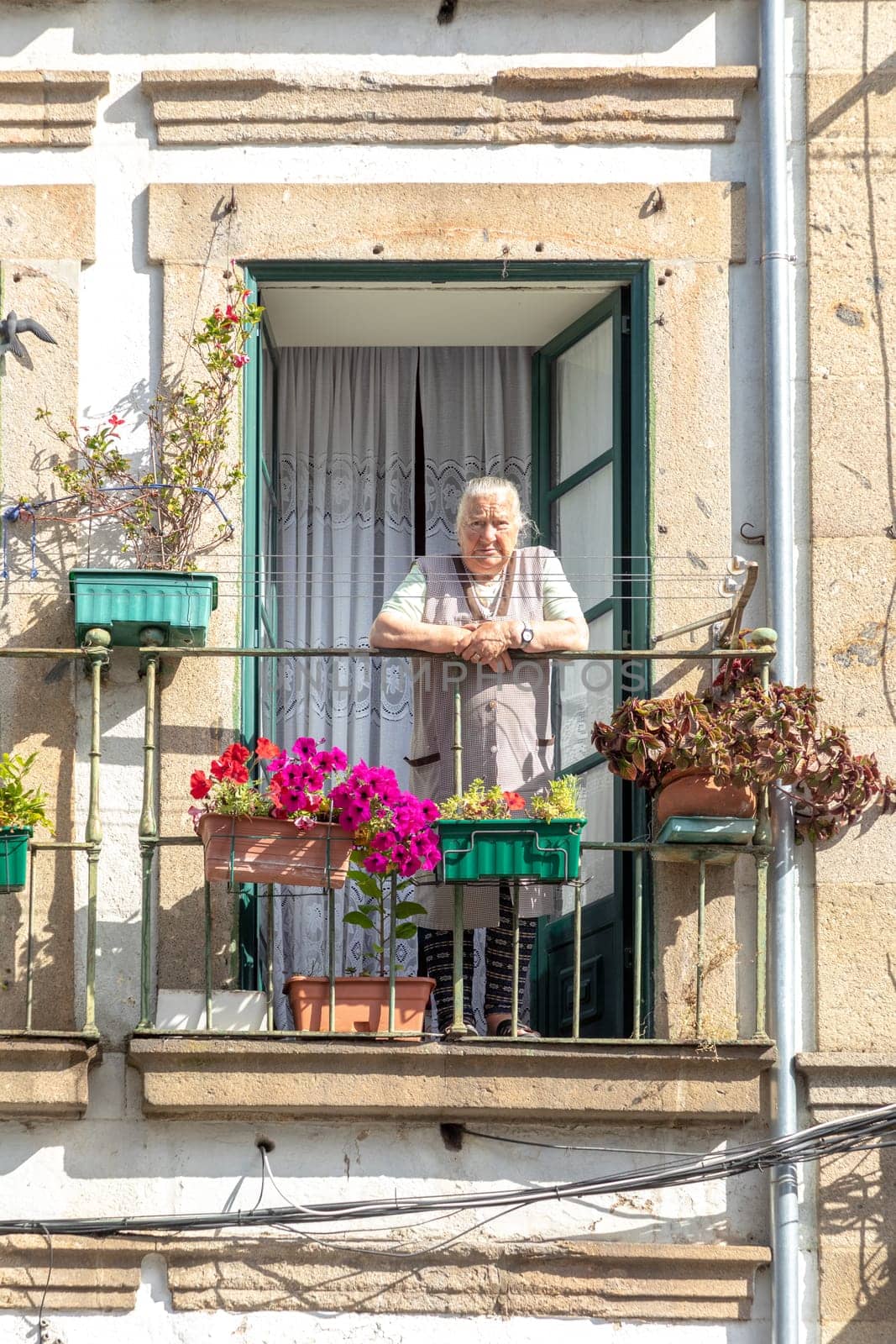 Braga, Portugal - May 1, 2023: elderly lady watches the street from her balcony in the old town of Braga, Portugal.