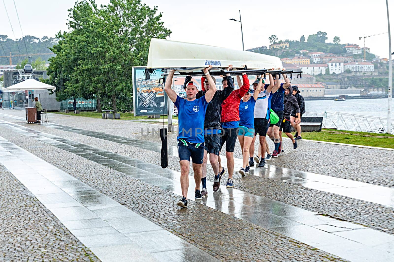 Porto, Portugal - May 3, 2023: rowers in  team of eight carry the rowboat to the rowboat hall in heavy rain in Porto.