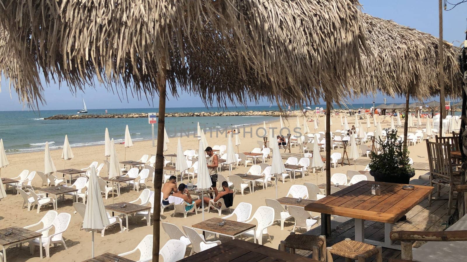 Tel Aviv, Israel - May 21, 2023: people enjoy the beach in Tel Aviv and sit under bamboo parasols and relax at beach couches in the midday heat.