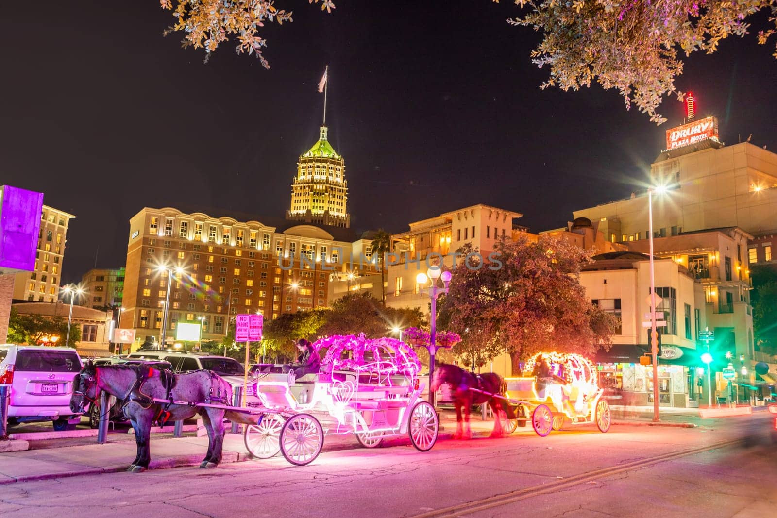 San Antonio, USA - October 31, 2023:  people enjoy to have a ride by night in the horse drawn carriage with colorful neon light in San Antonio at the river walk area.