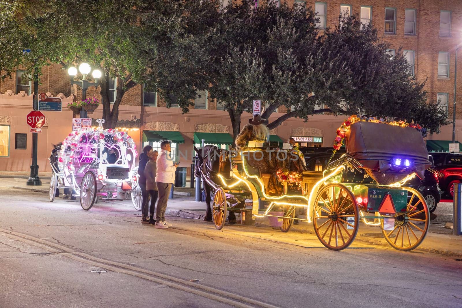 San Antonio, USA - October 31, 2023:  people enjoy to have a ride by night in the horse drawn carriage with colorful neon light in San Antonio at the river walk area.