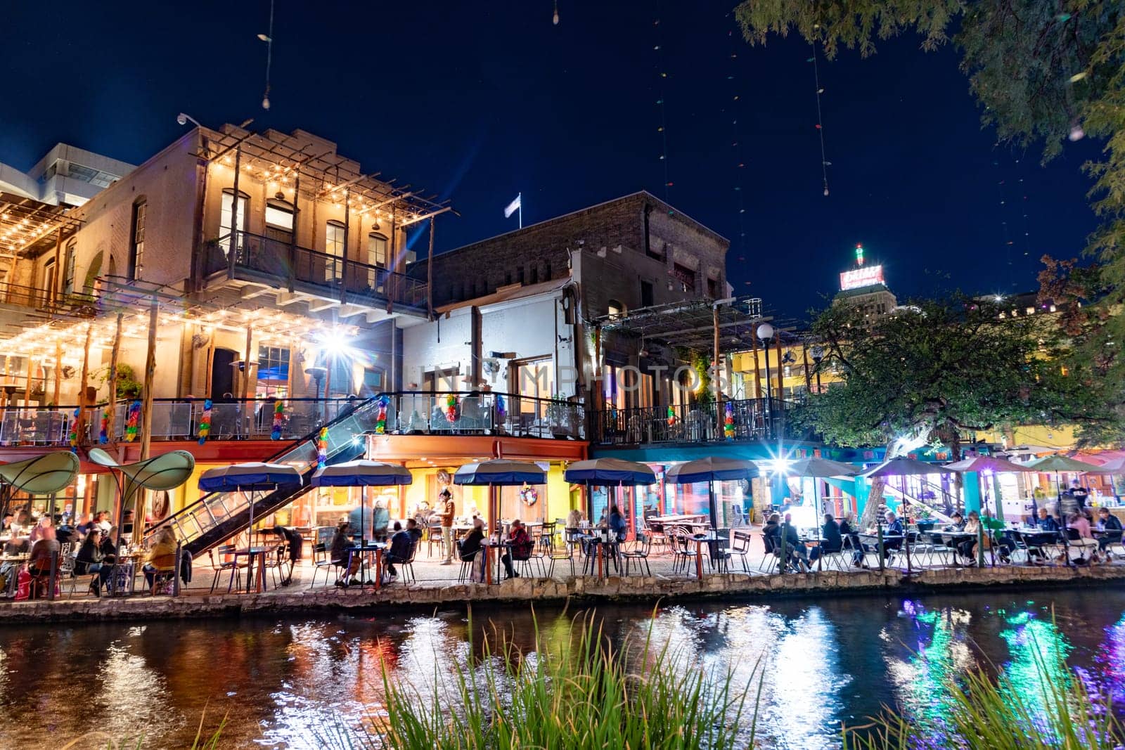 San Antonio, USA - October 31, 2023:  people enjoy the evening at the San Antonio River Walk with costumes by night and illuminated trees and restaurants.