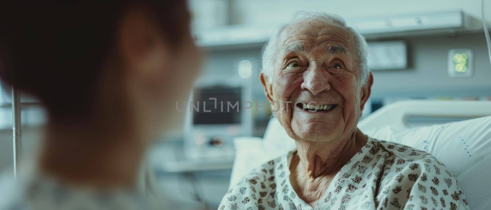 An elderly man in a hospital gown beams with a broad smile during a pleasant conversation. The warmth of the exchange fills the hospital room
