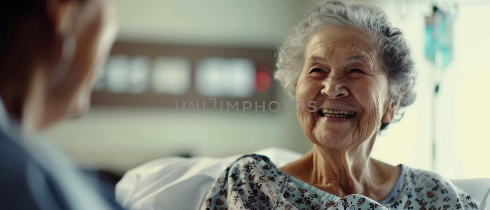 A senior woman's warm smile fills the hospital room as she chats with a caregiver, her spirit undiminished by her surroundings