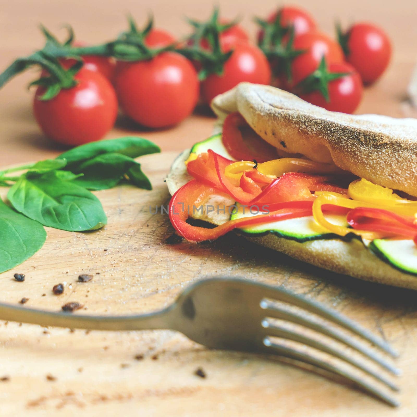 Veggie closed pizza. Peppers and zucchini. On background small red tomatoes, mozzarella and basil. Fork. Selective focus. Vintage color palette.