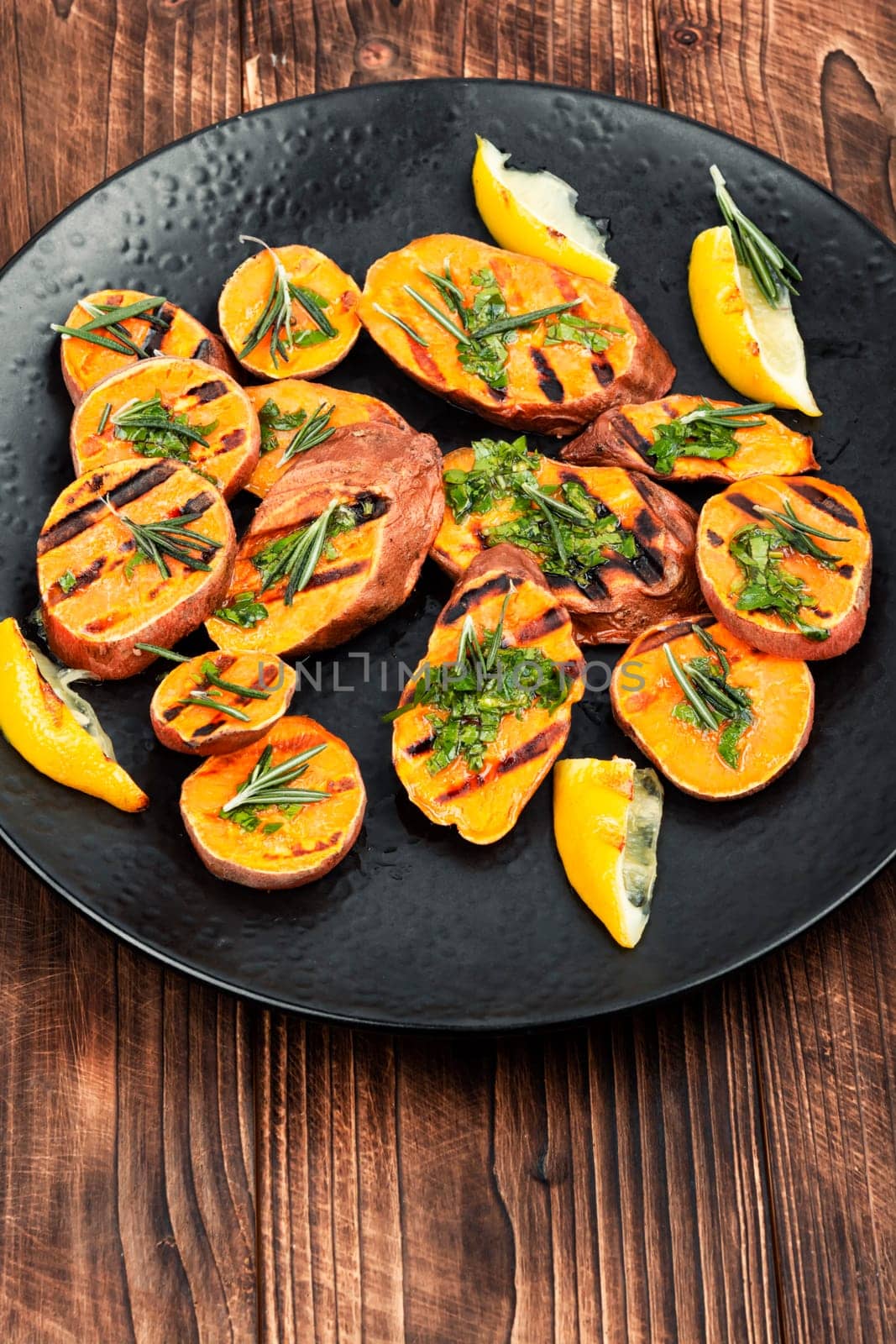 Homemade grilled sweet potato, batata with herbs on old rustic wooden table.
