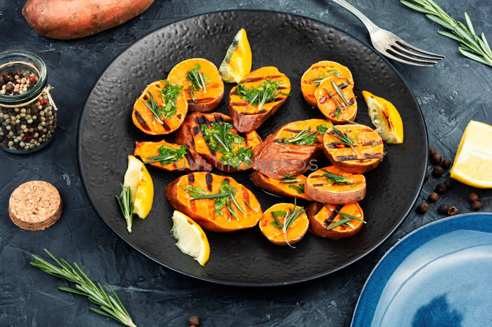 Homemade grilled sweet potato, batata with herbs on old rustic wooden table.