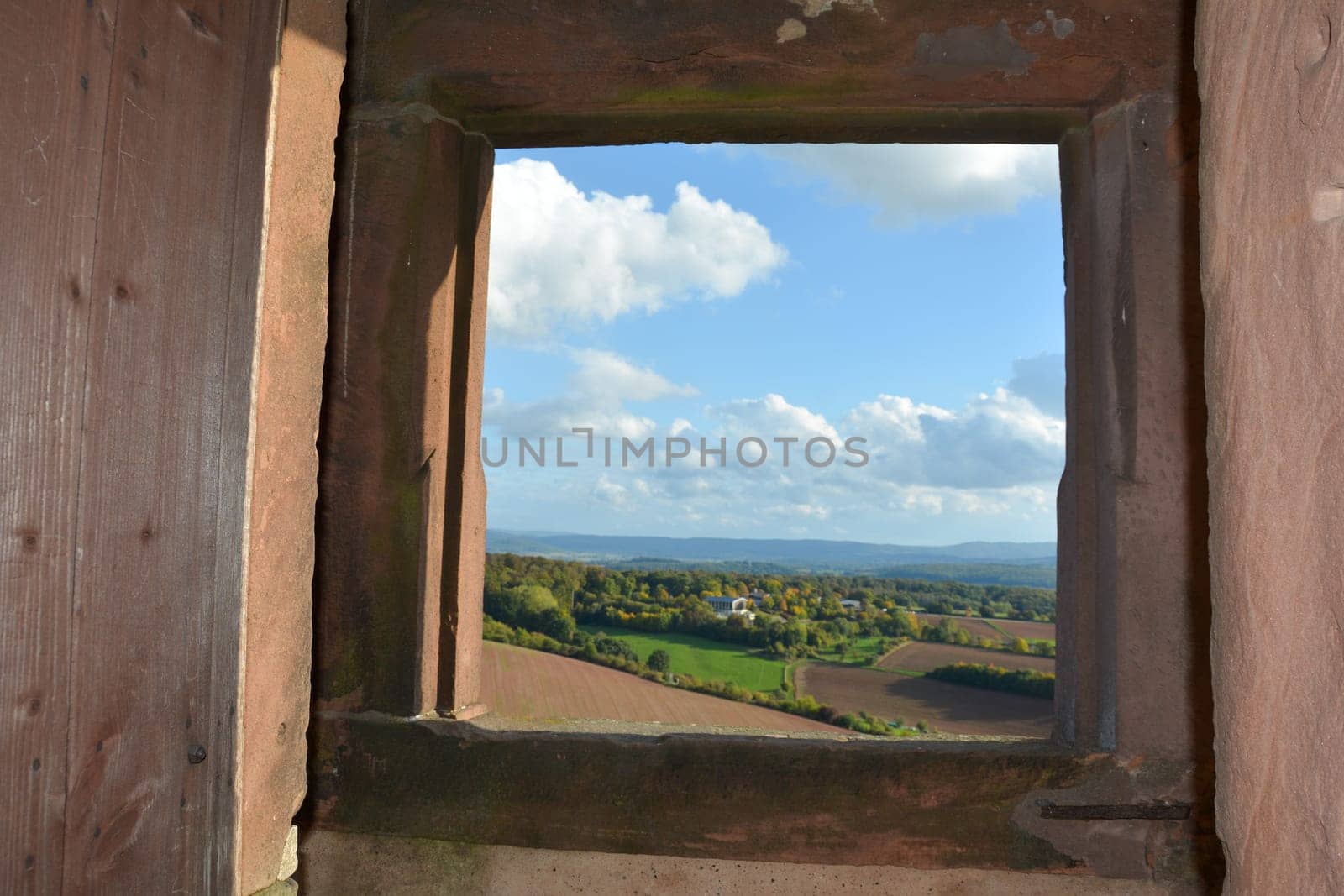 View through an old castle window on a blue sky with white clouds and green landscape