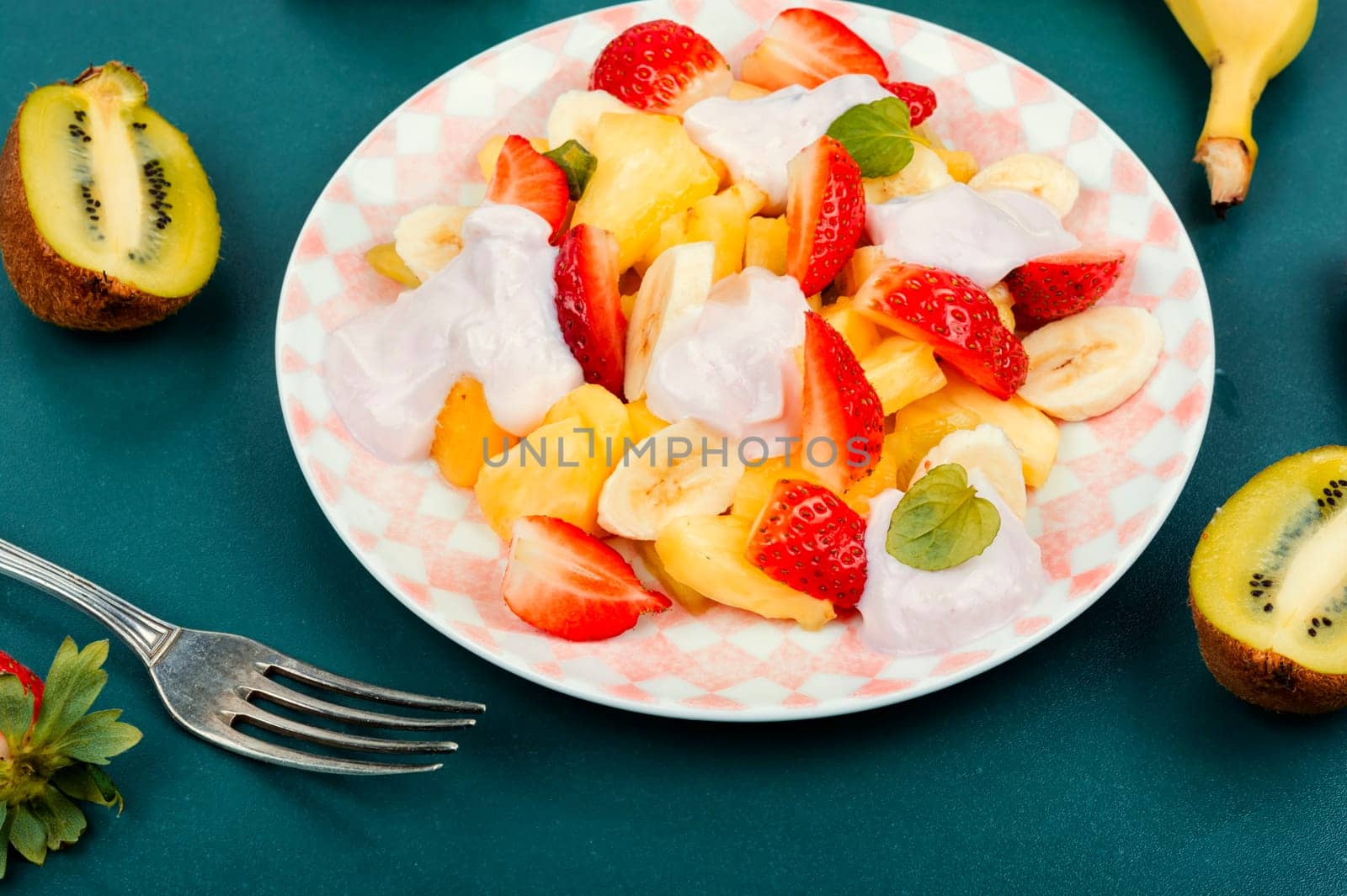 Summer fruit salad of pineapple, strawberries, kiwi and yogurt on a plate.