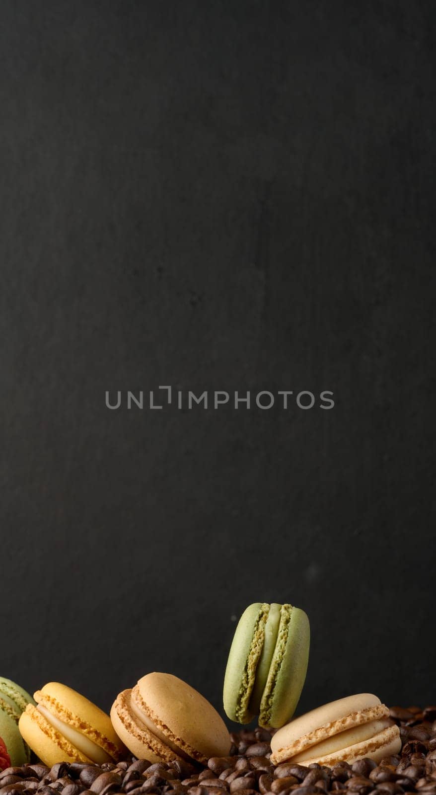 Stack of multi-colored macarons on a background of coffee beans, black background