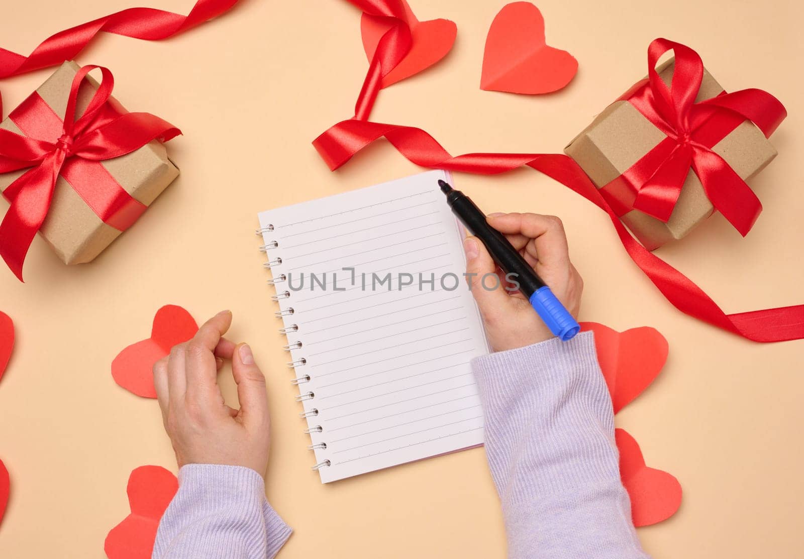 Open notebook with empty white sheets and gift boxes around on a yellow background, top view. Festive background for wish
