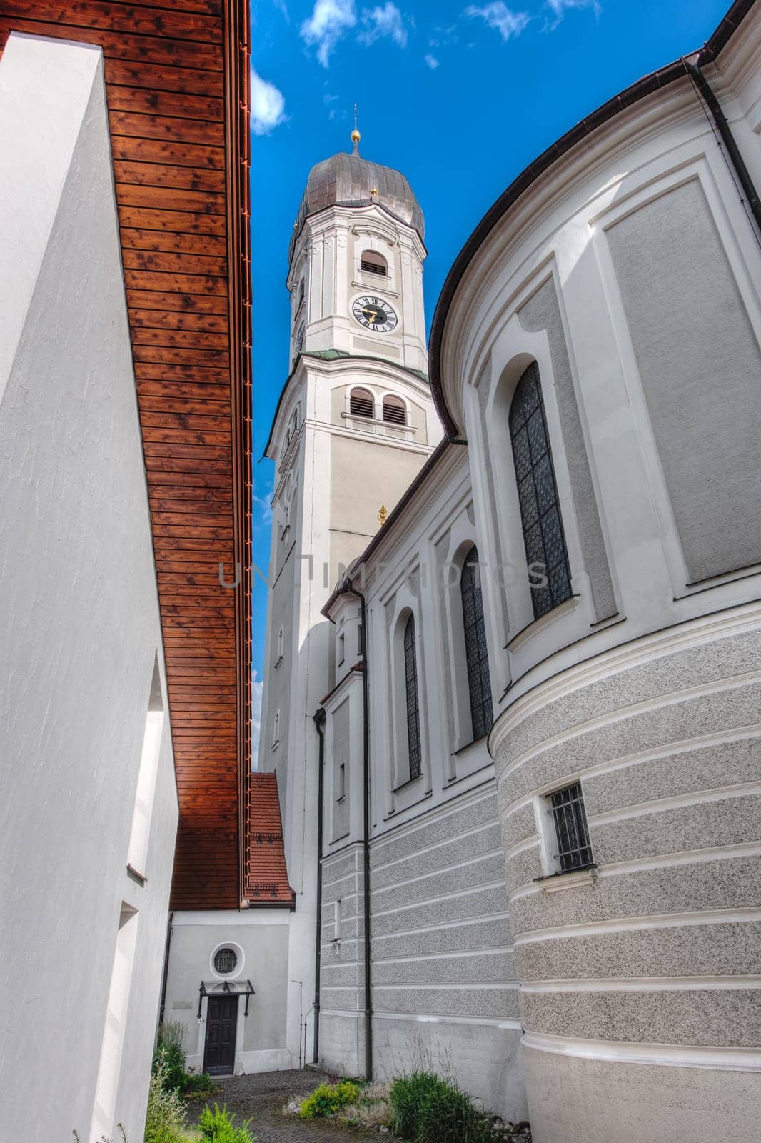 Wide-angle view of the bell tower with access to the tower chapel of the Saint Andreas Church in Nesselwang Bavaria from the west against a blue sky with small clouds in summer 2023.