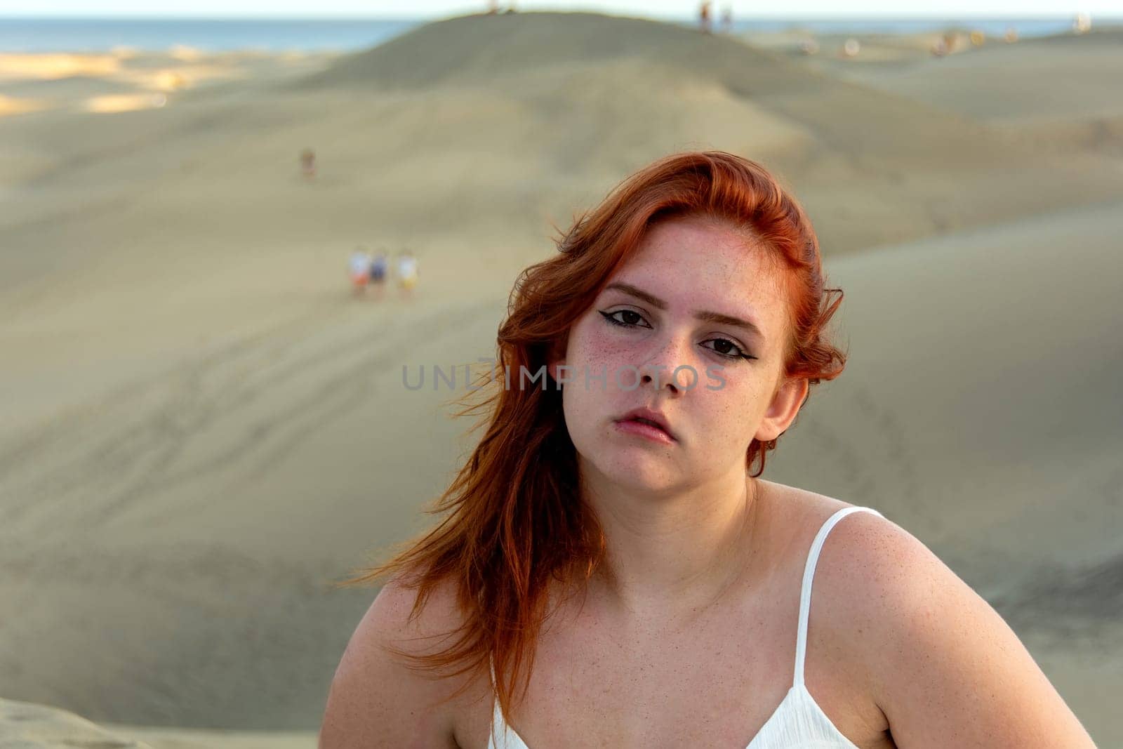 Young girl with red hair, on the beach in summer, her hair tousled by the wind