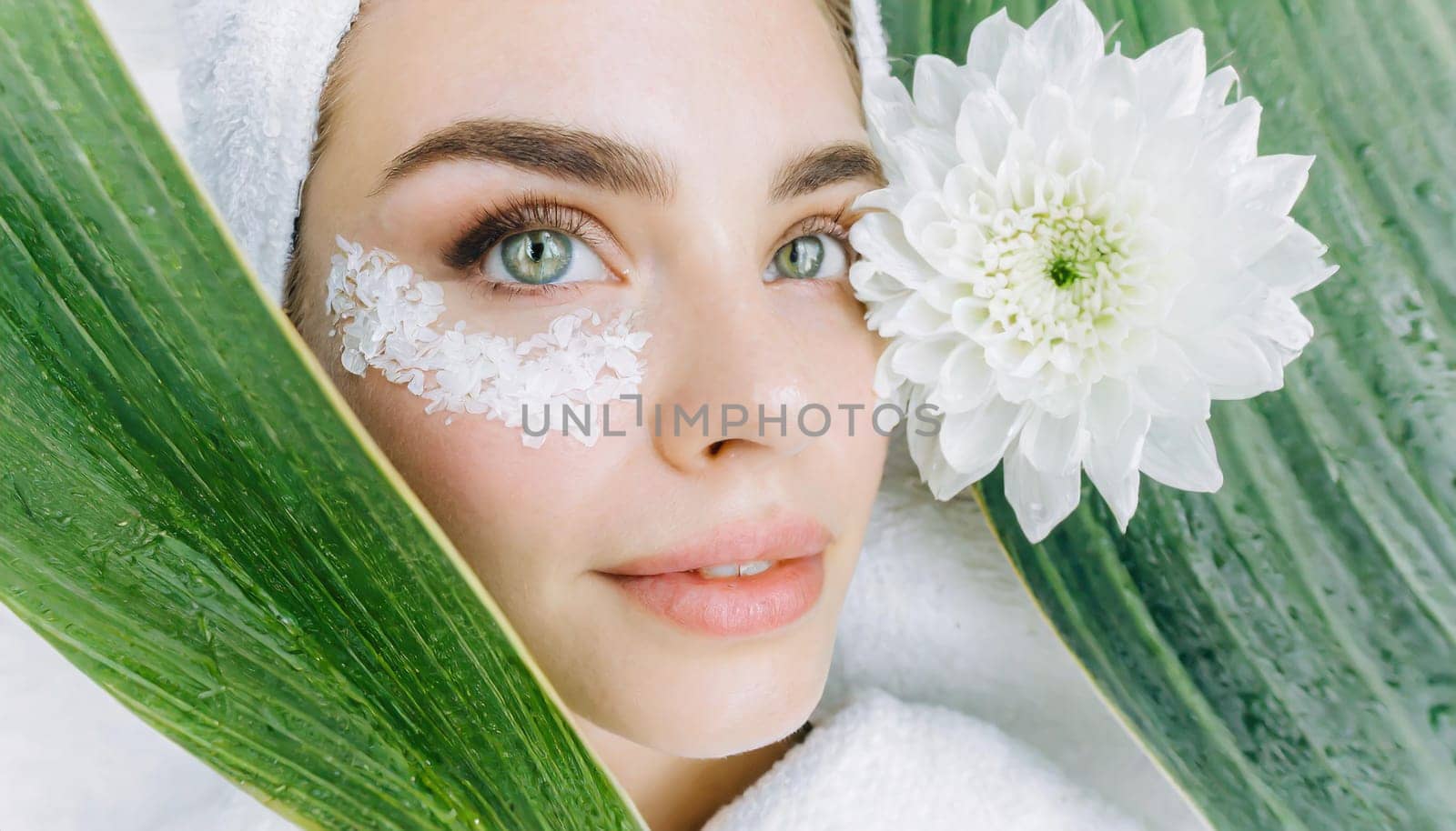 Portrait of beautiful woman with healthy glow perfect smooth skin holds tropical leaf, look into the hole of green paper. Young girl enjoys cream facial mask. Fashion, beauty, skincare concept.