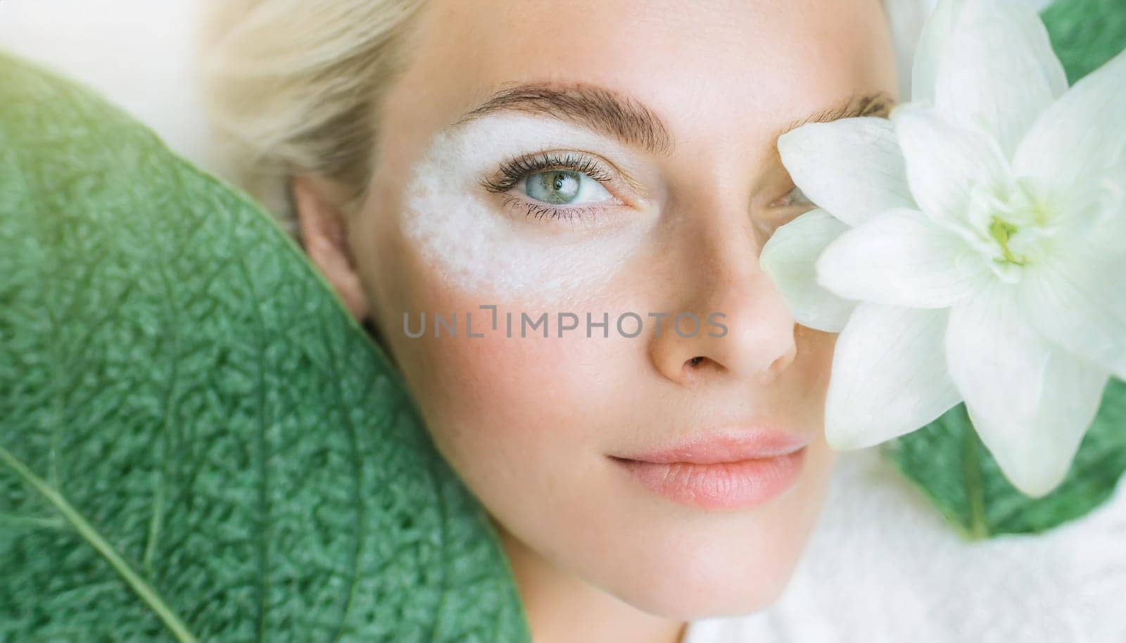 Portrait of beautiful woman with healthy glow perfect smooth skin holds tropical leaf, look into the hole of green paper. Young girl enjoys cream facial mask. Fashion, beauty, skincare concept.