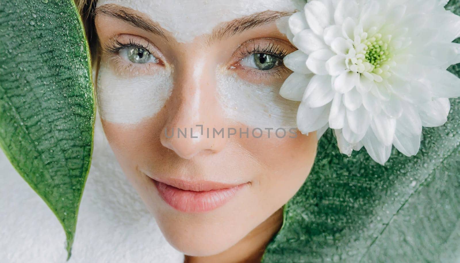 Portrait of beautiful woman with healthy glow perfect smooth skin holds tropical leaf, look into the hole of green paper. Young girl enjoys cream facial mask. Fashion, beauty, skincare concept.