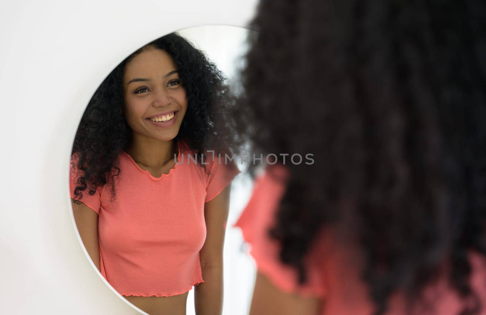 Portrait of young african happiness woman in orange t-shirt standing and looking in the mirror proud of herself at home