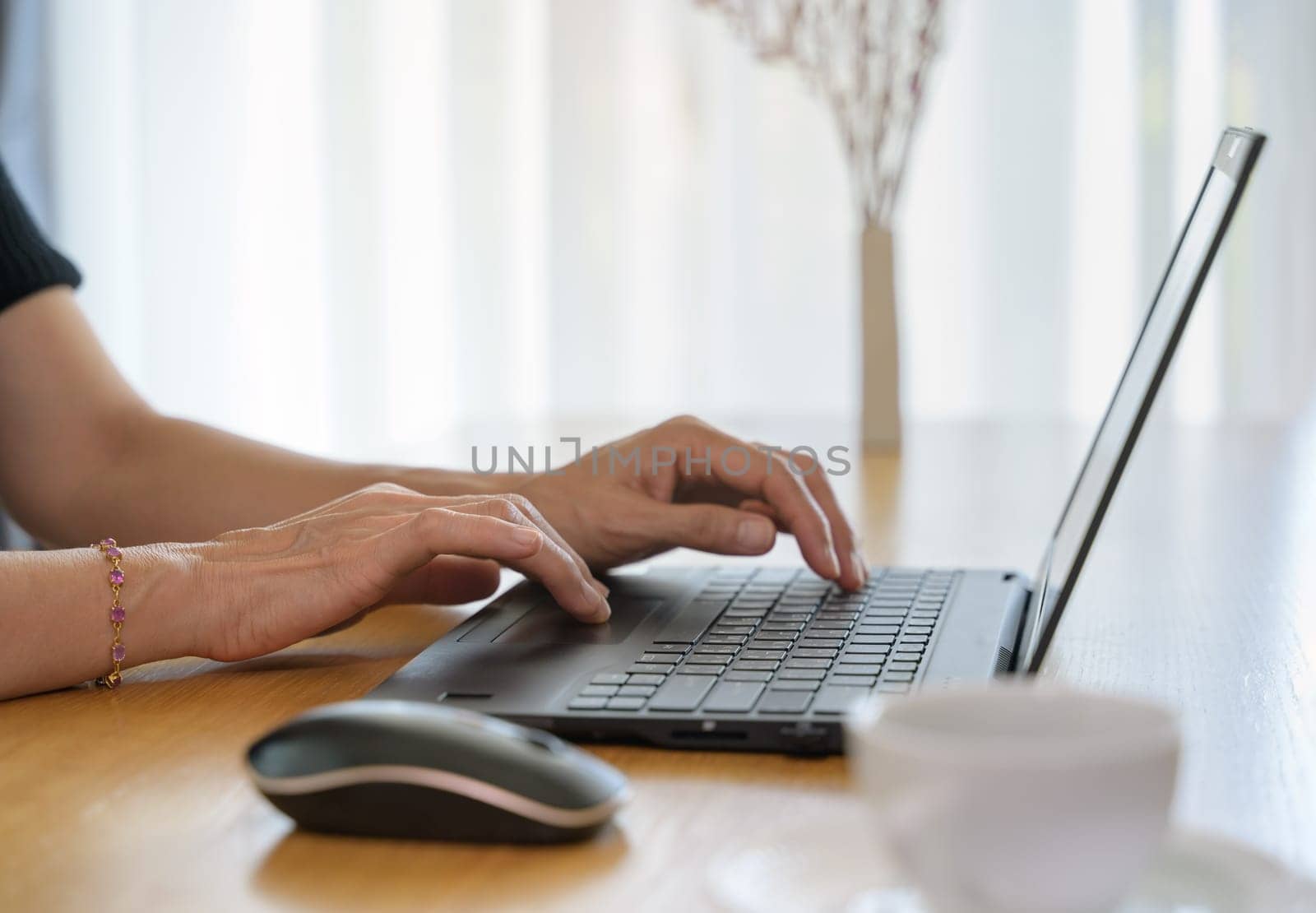 Woman using laptop computer while typing on her notebook while working online from home.
