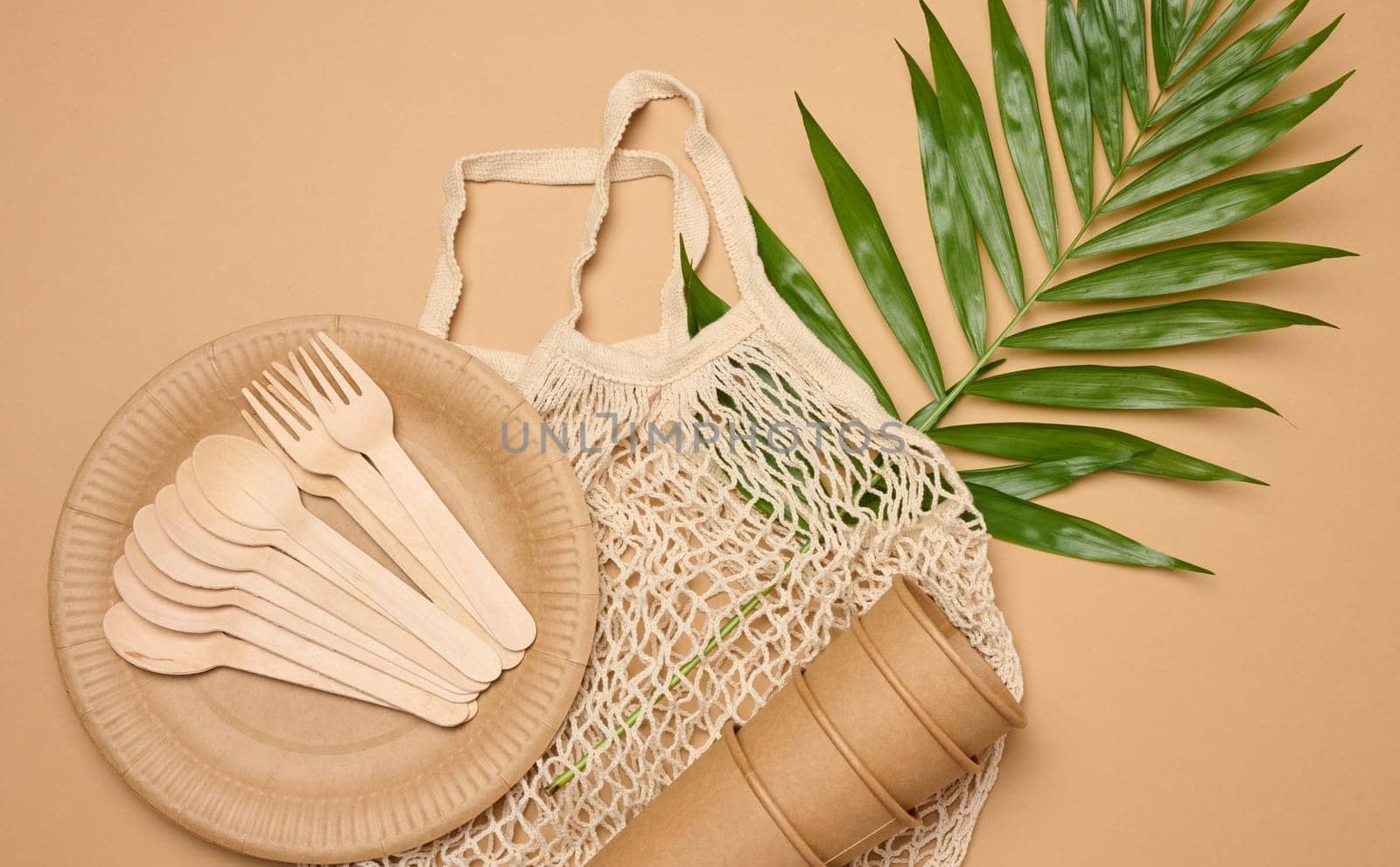 Paper plates and cups, wooden spoons and forks on a beige background, top view