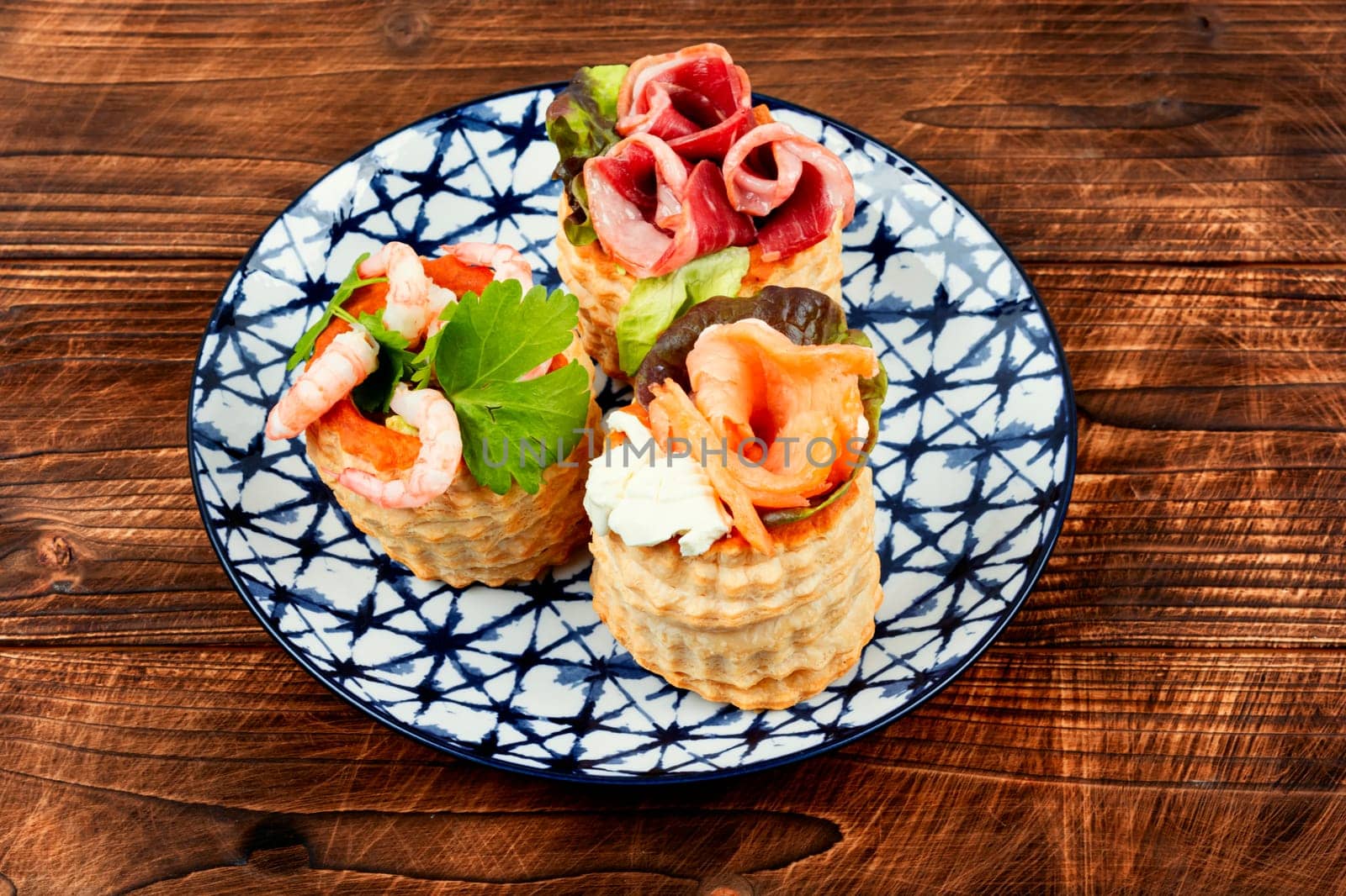 Puff pastry tartlets or canapes with fish, shrimp and bacon on a plate on the table.