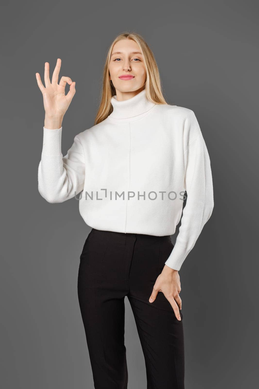 Young woman in trousers and sweater shows OK gesture