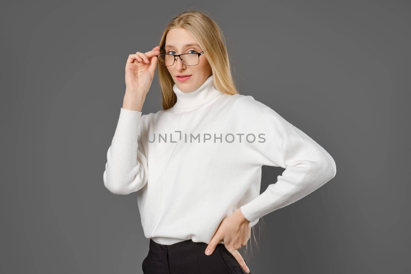 Young serious woman holding glasses by the temple while looking at the camera