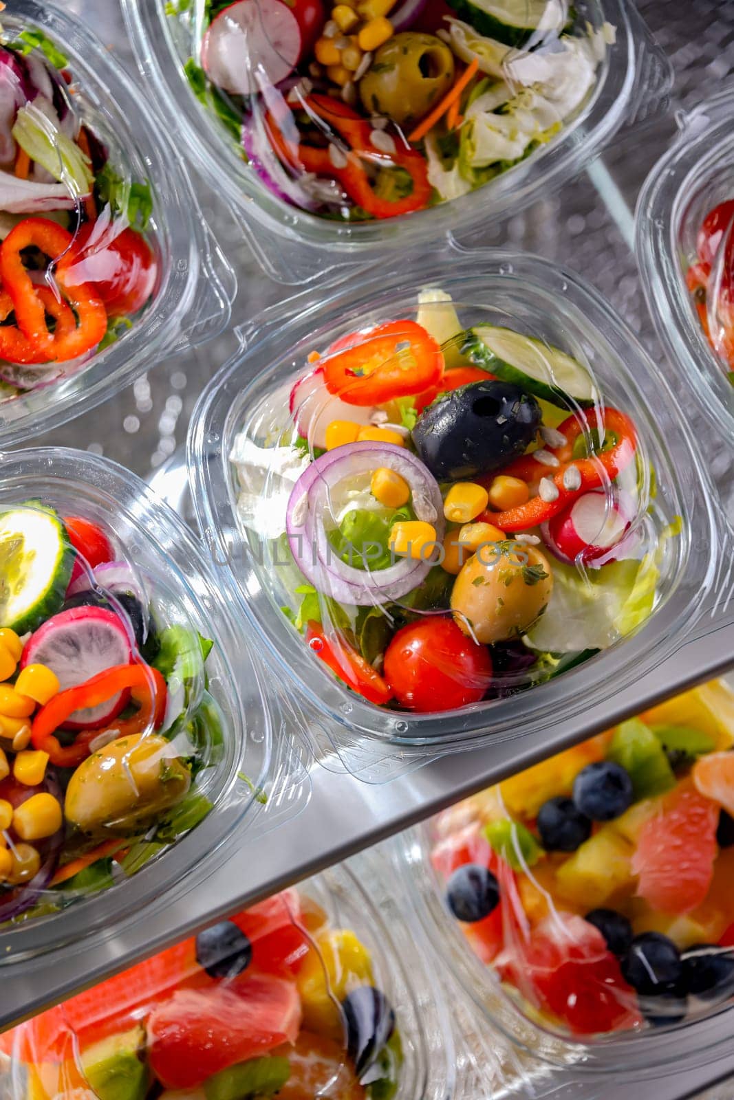 Plastic boxes with pre-packaged vegetable salads, put up for sale in a commercial refrigerator