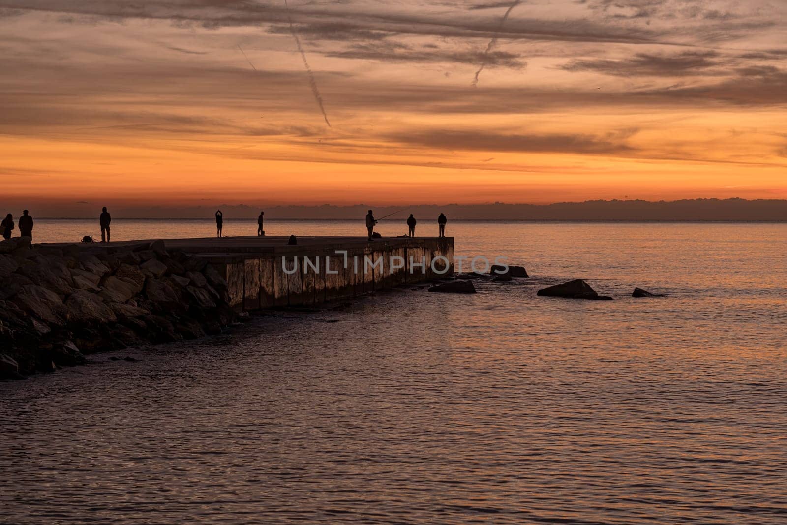 Mediterranean landscape at sunrise. People fishing, walking or exercising at the Espigó del Gas (Gas Breackwater), on the waterfront in Barcelona, Spain.