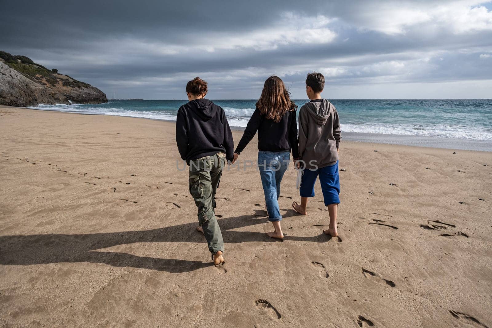 A parent and two young sons walking together along a deserted beach, rear view. Conceptual theme of doing fun things together and taking time to relax, reconnect within the family.