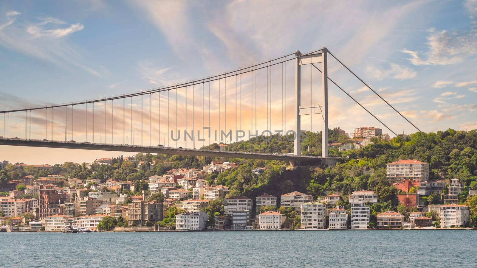 Bathed in the golden hues of sunset, the Bosphorus Bridge casts a mesmerizing reflection on the shimmering waters below, Istanbul, Turkey
