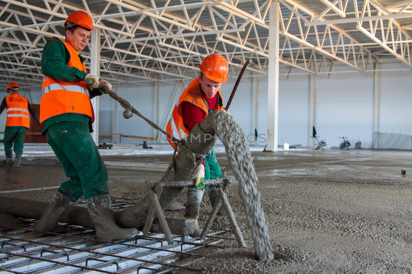 two Caucasian workers pouring concrete floor in large industrial hangar building in Tula, Russia - July 22, 2013