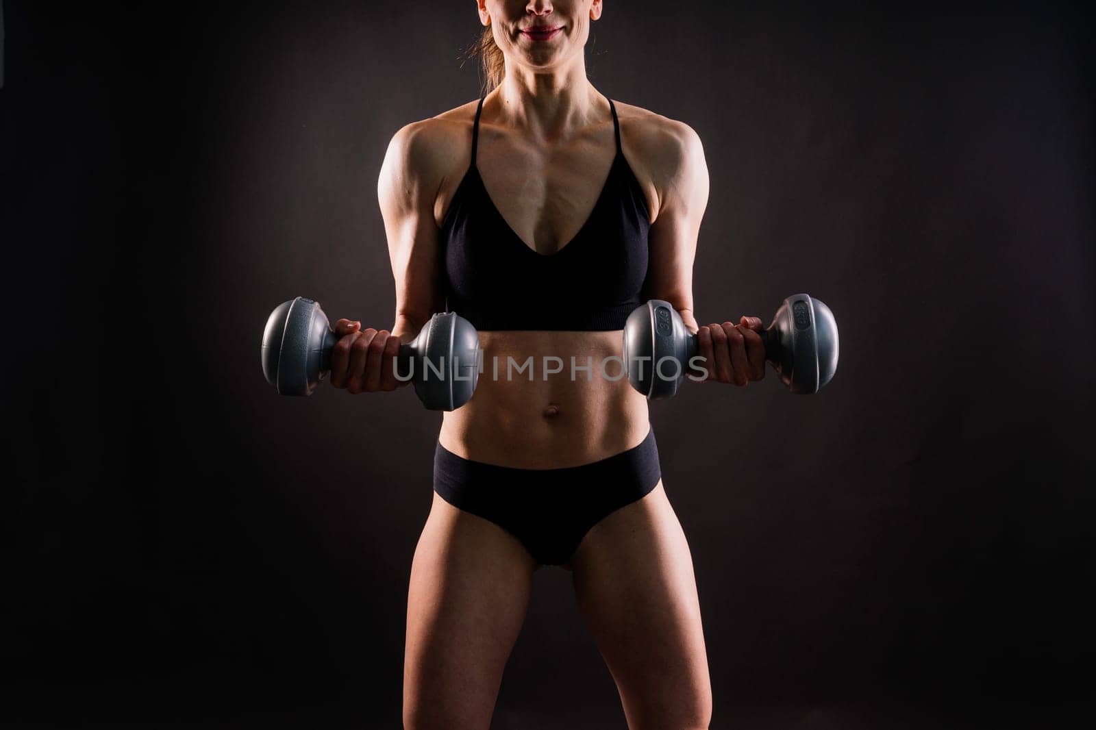 Sporty female doing exercise with a dumbbells, silhouette studio shot dark yellow background
