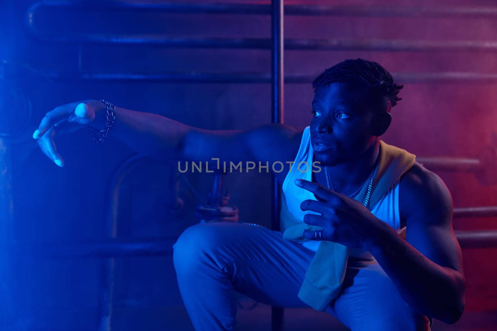 Young cool guy rapper posing for camera in neon light. Sportive millennial boy hip-hop dancer in stylish street style clothes portrait