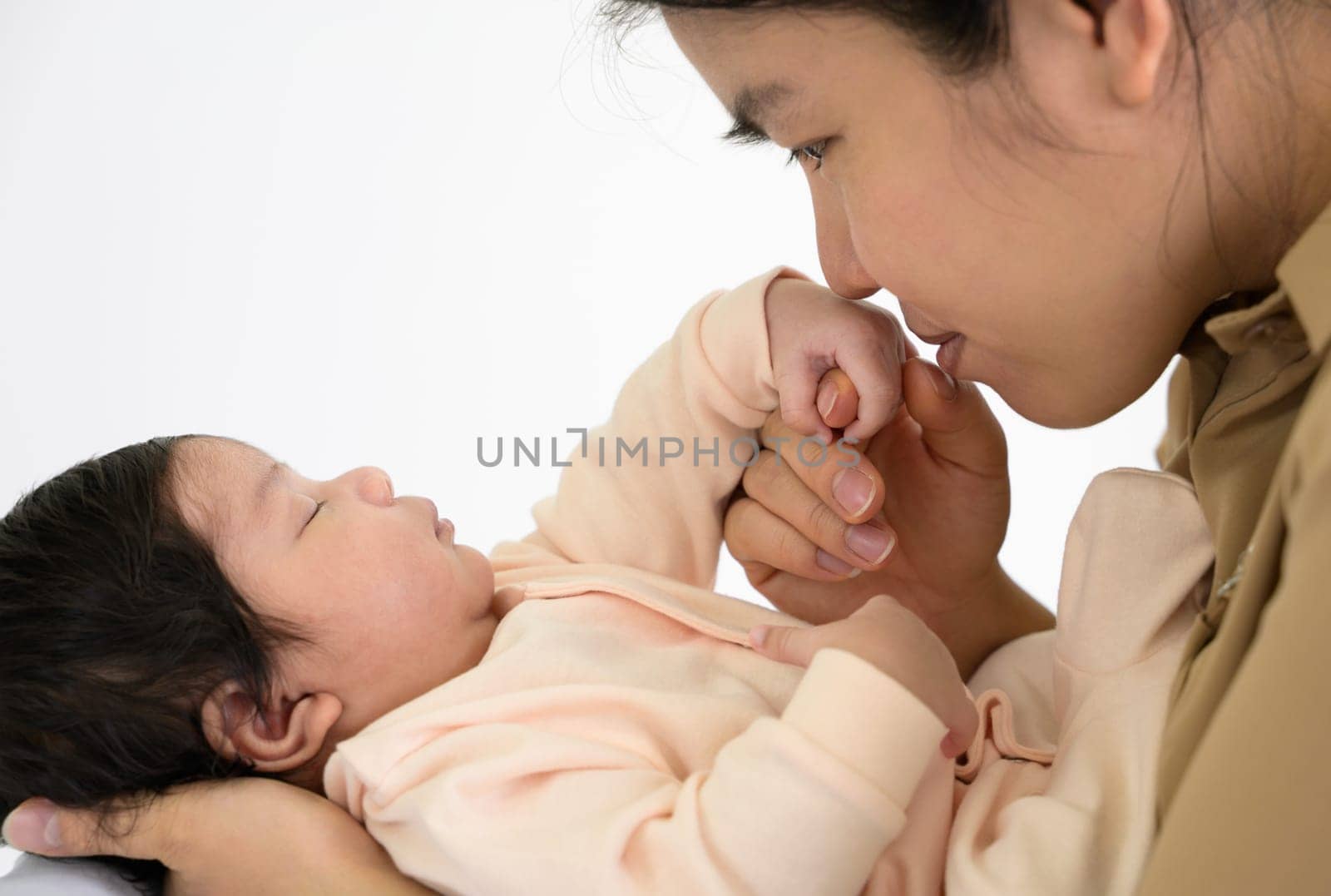 Adorable newborn baby sleeping in tender hand of mother at home. Asian happy mom holding and gently kissing hand of infant girl or boy with love. Care, love and mothers day