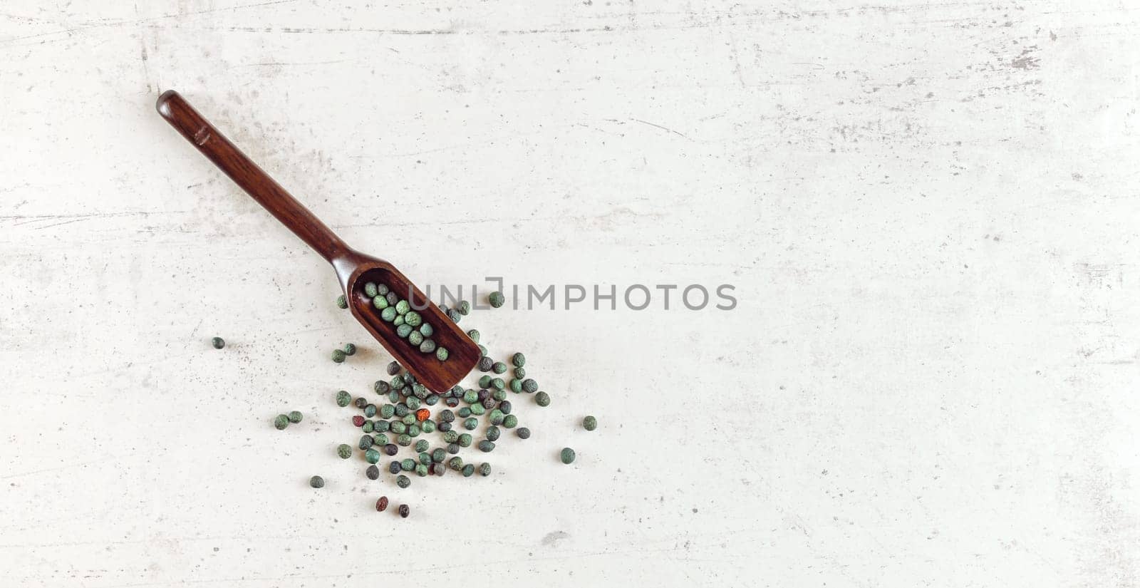 Small blue green peppercorns in dark wooden spoon on white stone like table
