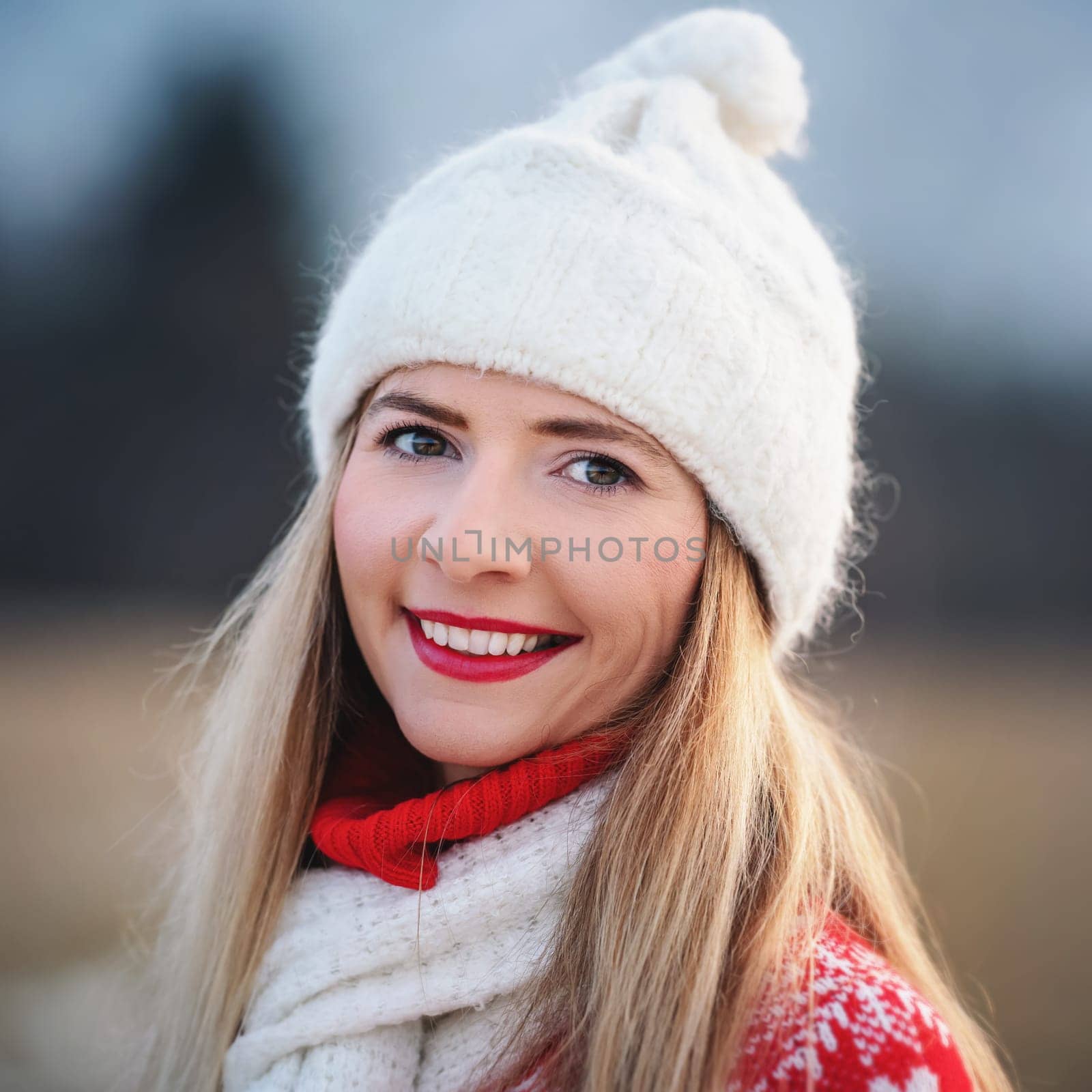 Portrait of young woman in white winter hat and red jumper, closeup to her smiling face
